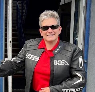 Image of a woman with short hair, smiling, wearing a red shirt and black jacket and wearing black sunglasses