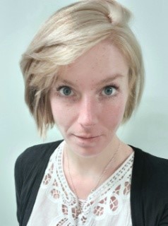 A woman with short, blond hair, wearing a cream blouse and black cardigan.