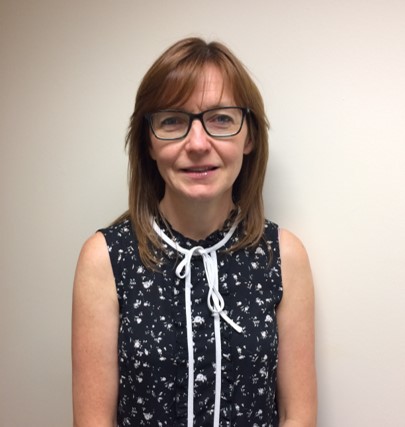 A woman with glasses, short brown hair, wearing a sleeveless black blouse.