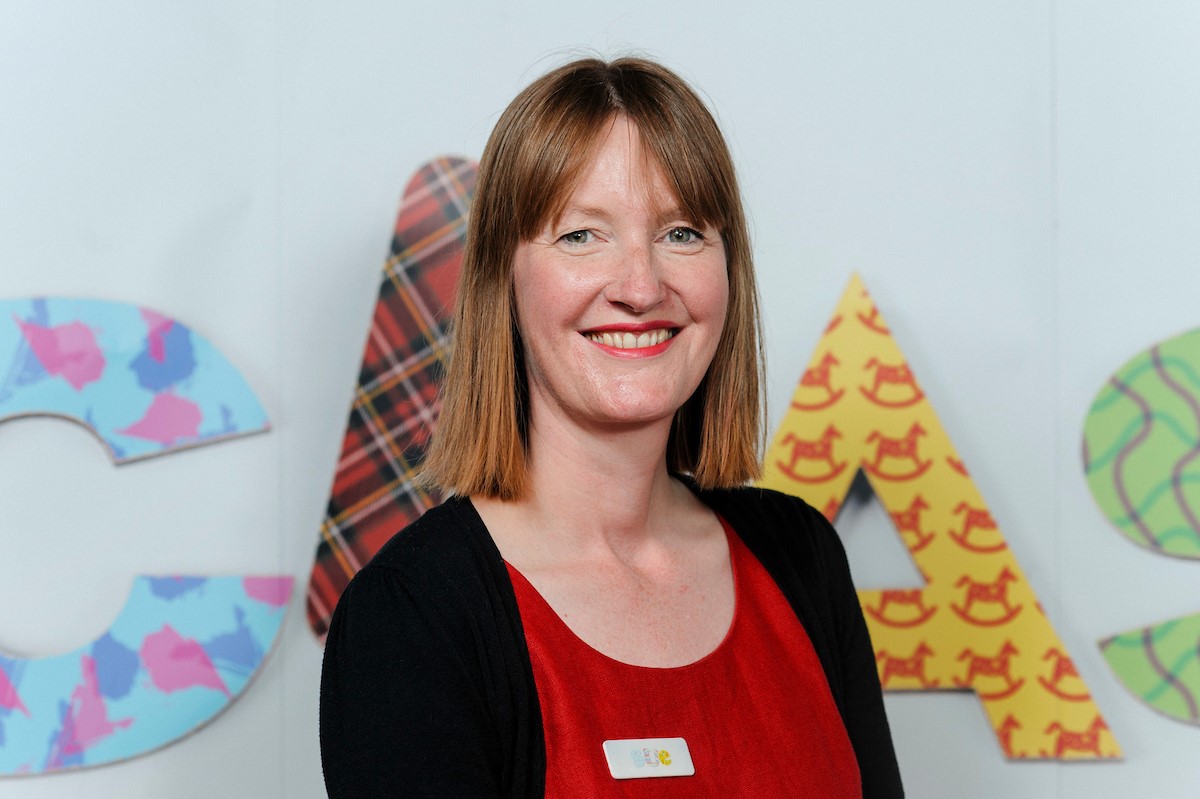 A woman with short brown hair, wearing a red top and a black cardigan.