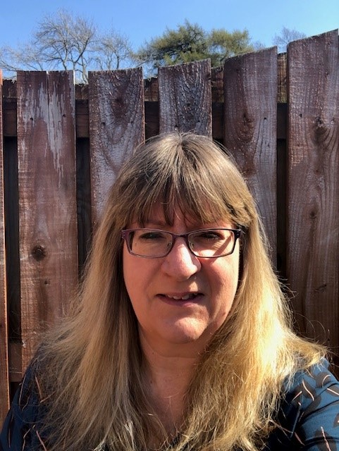 A woman with long brown/blond hair, wearing glasses.