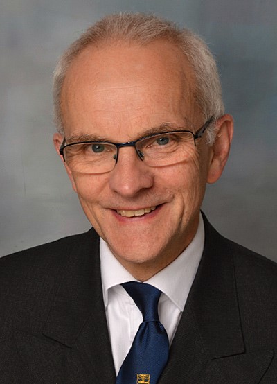 A man with glasses, wearing a dark suit.