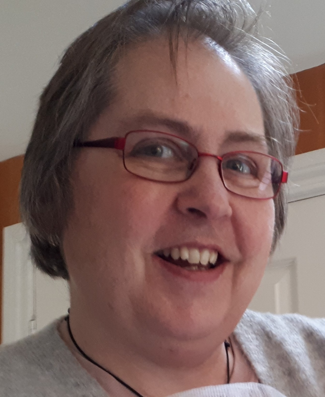 A woman with short grey hair, wearing glasses.