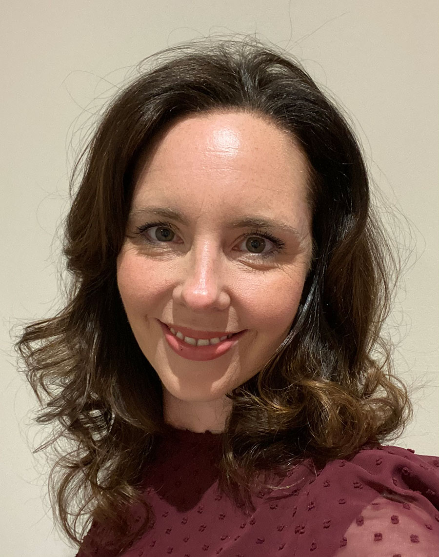 A woman with curly brown hair, wearing a maroon blouse.