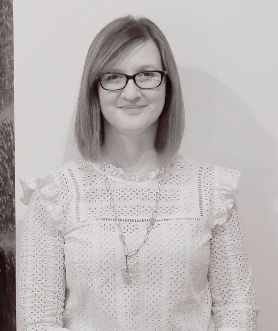 A woman with shoulder length hair, wearing a light blouse.