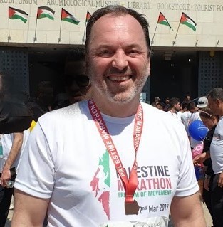 A man smiling, wearing a white t-shirt and marathon medal