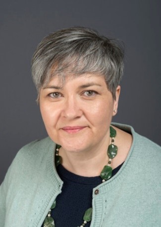 A woman with short grey hair, wearing a dark top and light blue cardigan