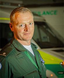 A man in a green paramedic's uniform standing in front of an ambulance.