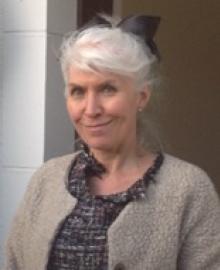 A woman with grey hair tied up, and a taupe cardigan.