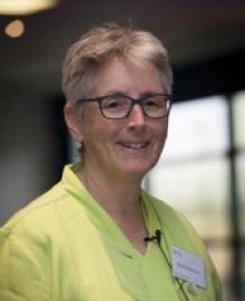 A woman with cropped blond hair, glasses and a yellow top.