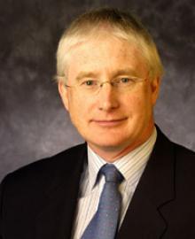 A man with blond hair, glasses and a black suit.