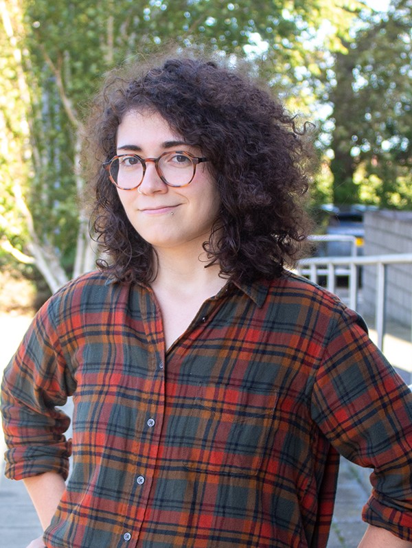 A woman with curly dark hair, wearing a dark checked shirt.