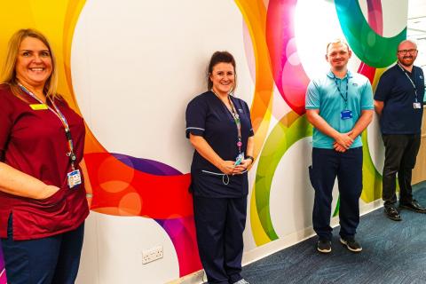 A group of people standing against a colourful wall.