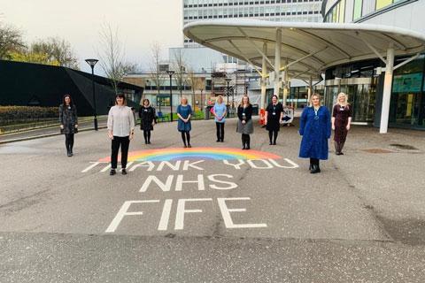 A group of people standing by a chalk drawing of a rainbow.