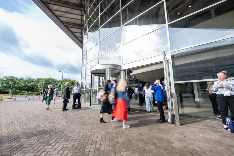 A photograph of the SEC building from the front, showing event attendees entering the building 