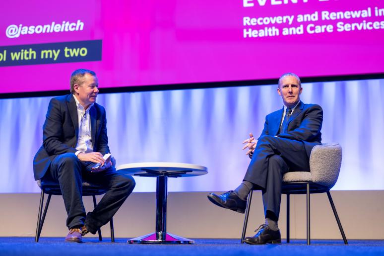 Two speakers sitting on the main stage delivering a presentation