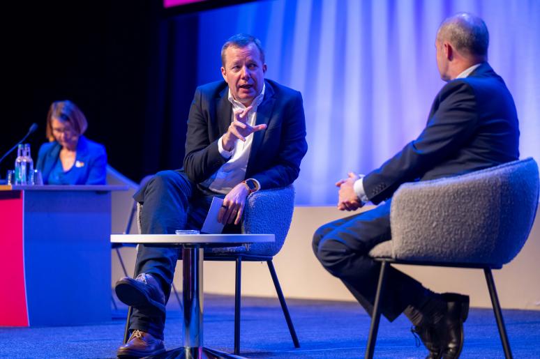 Two speakers sitting on the main stage delivering a presentation