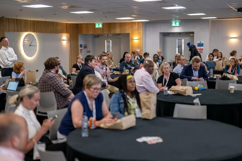 Multiple tables with event attendees sitting watching a presentation