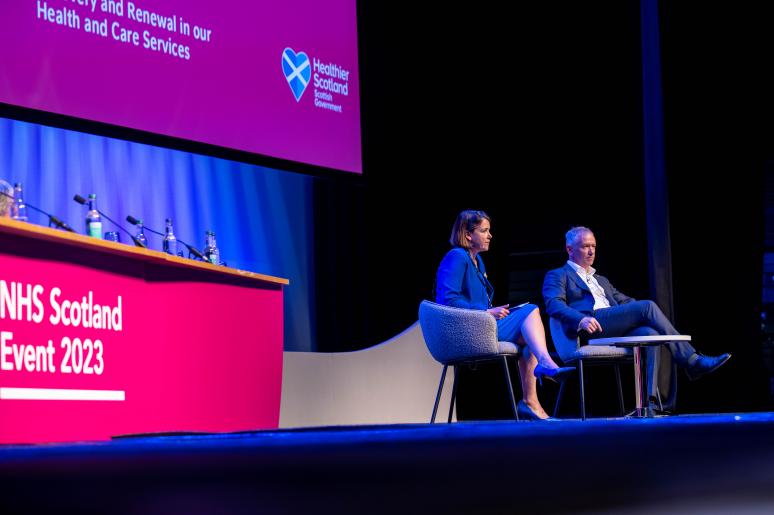 Two speakers sitting on the main stage delivering a presentation