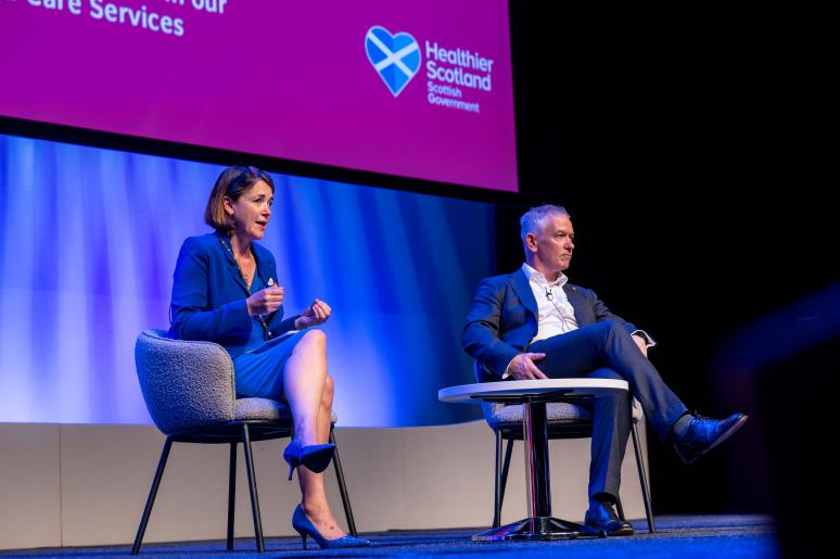 Two speakers sitting on the main stage delivering a presentation