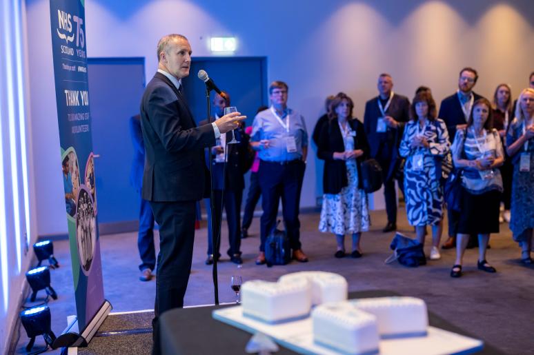A speaker giving a presentation and an audience in the background