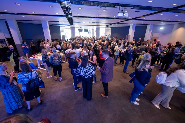 A wide-angle image of the event space with event attendees chatting before a presentation